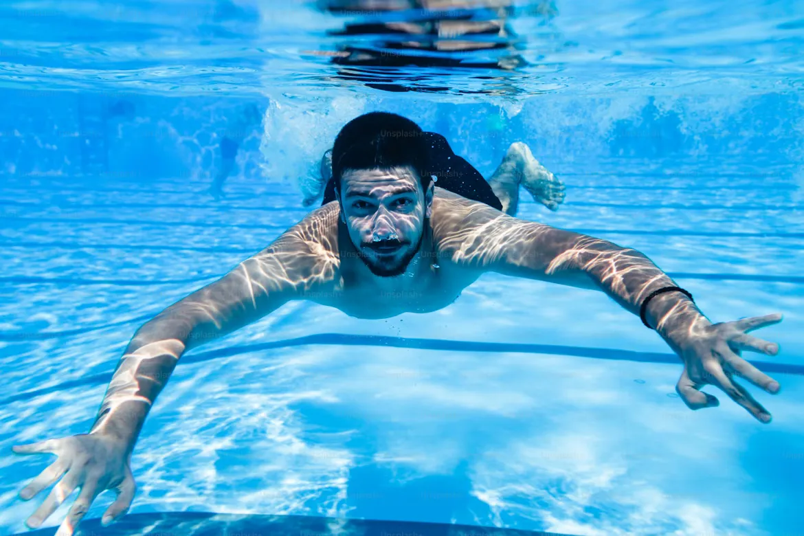 Underwater fun. Young handsome man swimming underwater and diving in the swimming poll.